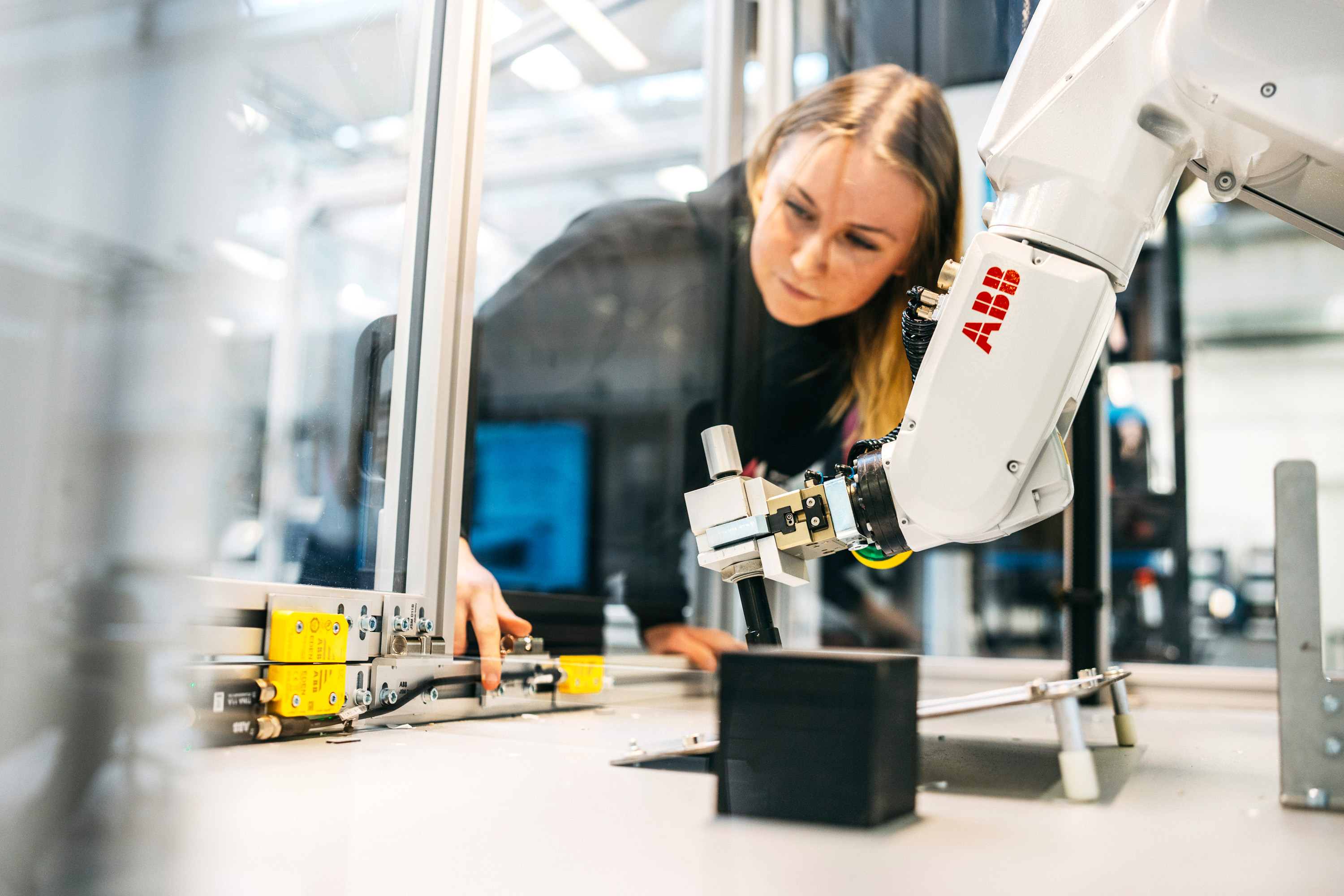 Kvinna som lutar sig in i ett dragskåp där en abb-robotarm utför arbete.